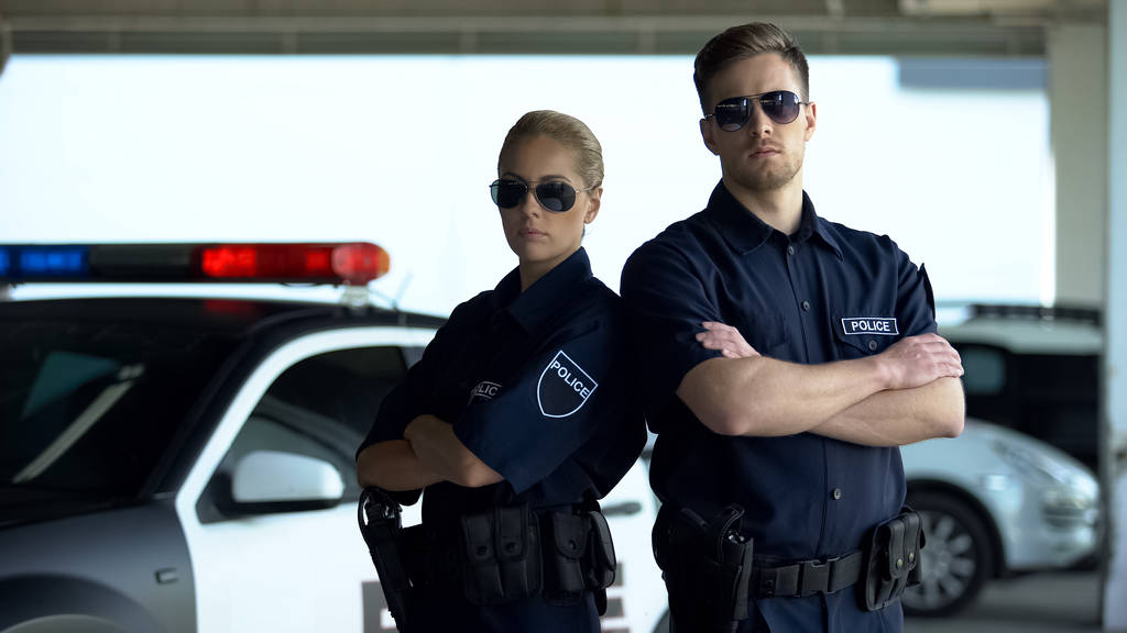 Brave politie vrouw en man in zonnebrillen staande met gevouwen handen in de buurt van auto - Foto, afbeelding