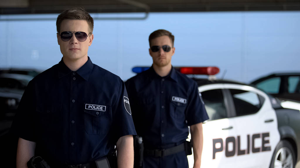 Чоловіки-офіцери в сонцезахисних окулярах, що стоять проти машини-загону, готові до патрулювання
 - Фото, зображення