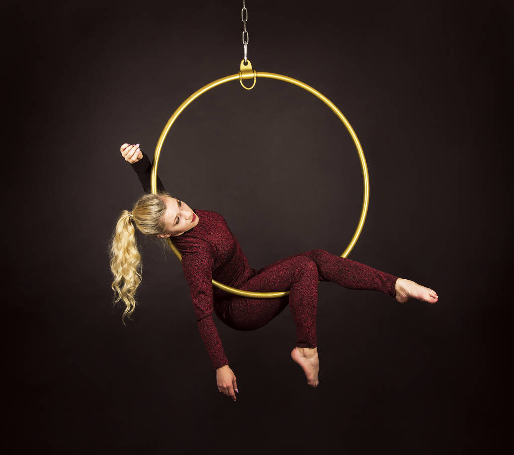 Uma menina loira esbelta-um acrobata de ar em um terno vermelho com cabelo longo, executa exercícios em um anel de ar
. - Foto, Imagem
