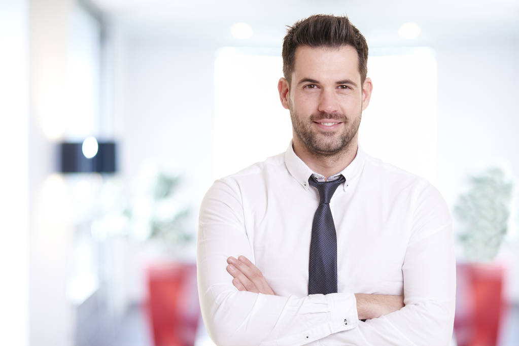 Portret foto van lachende zakenman dragen shirt en stropdas terwijl staan op kantoor en glimlachend.  - Foto, afbeelding
