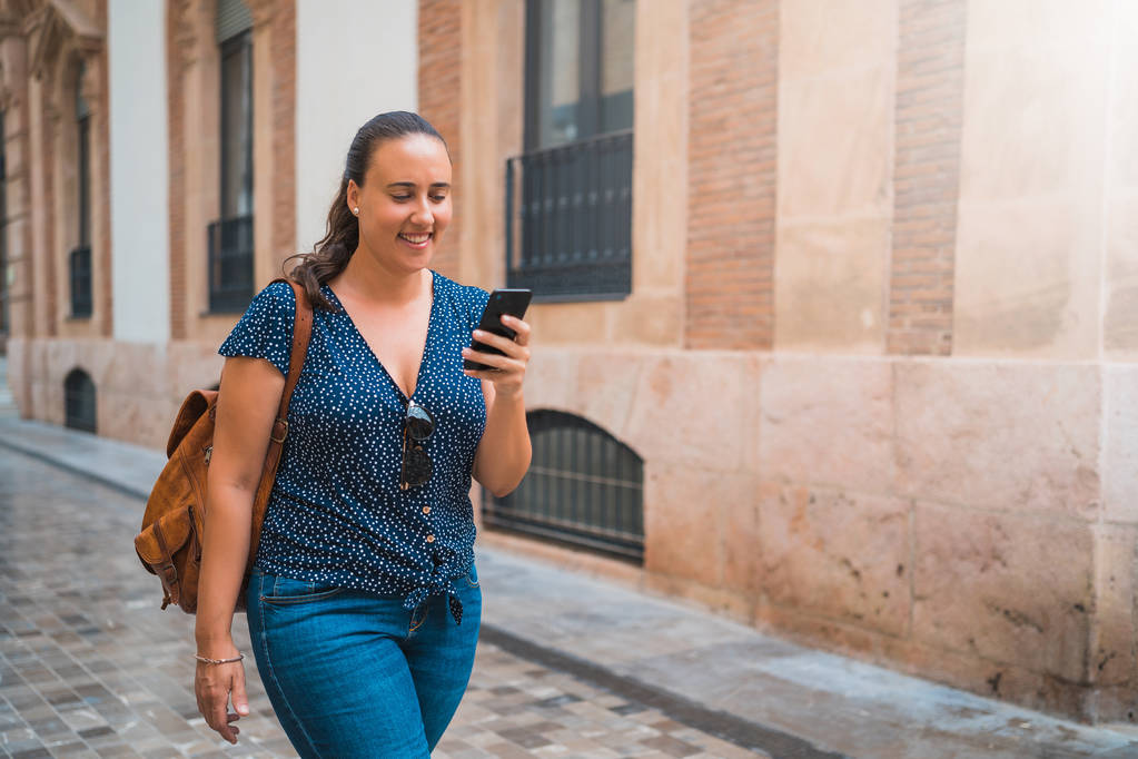 Nenucená mladá žena chodí a používá chytrý telefon na ulici města - Fotografie, Obrázek