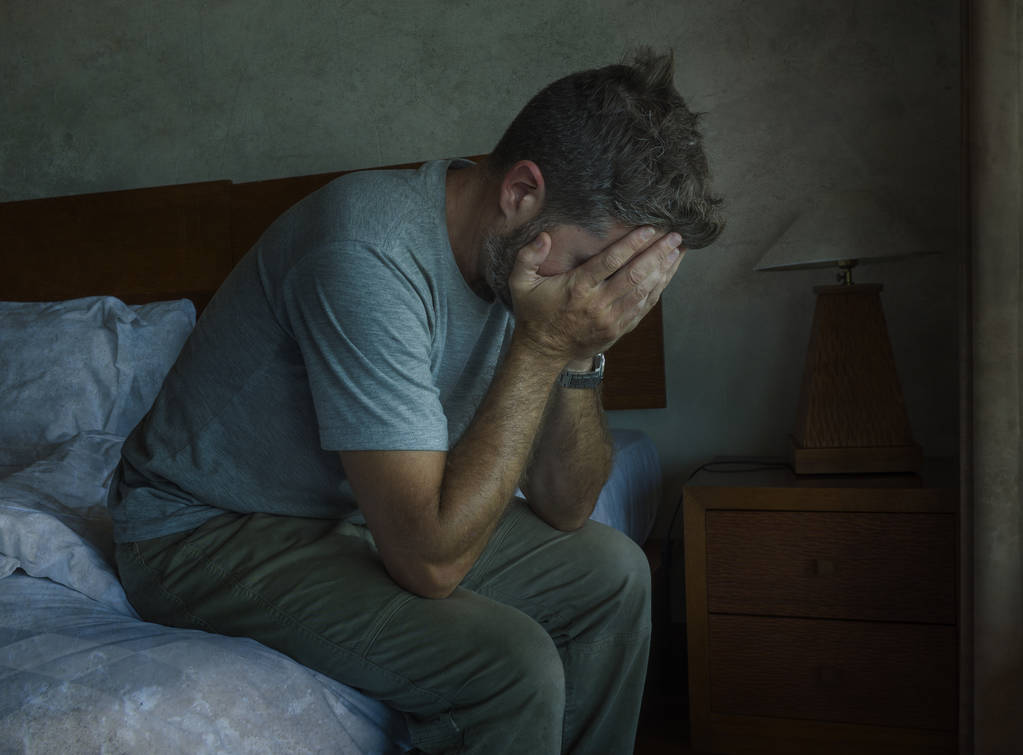 Attractive depressed and sad man at home sitting on bed crying desperate suffering depression problem  - Photo, Image