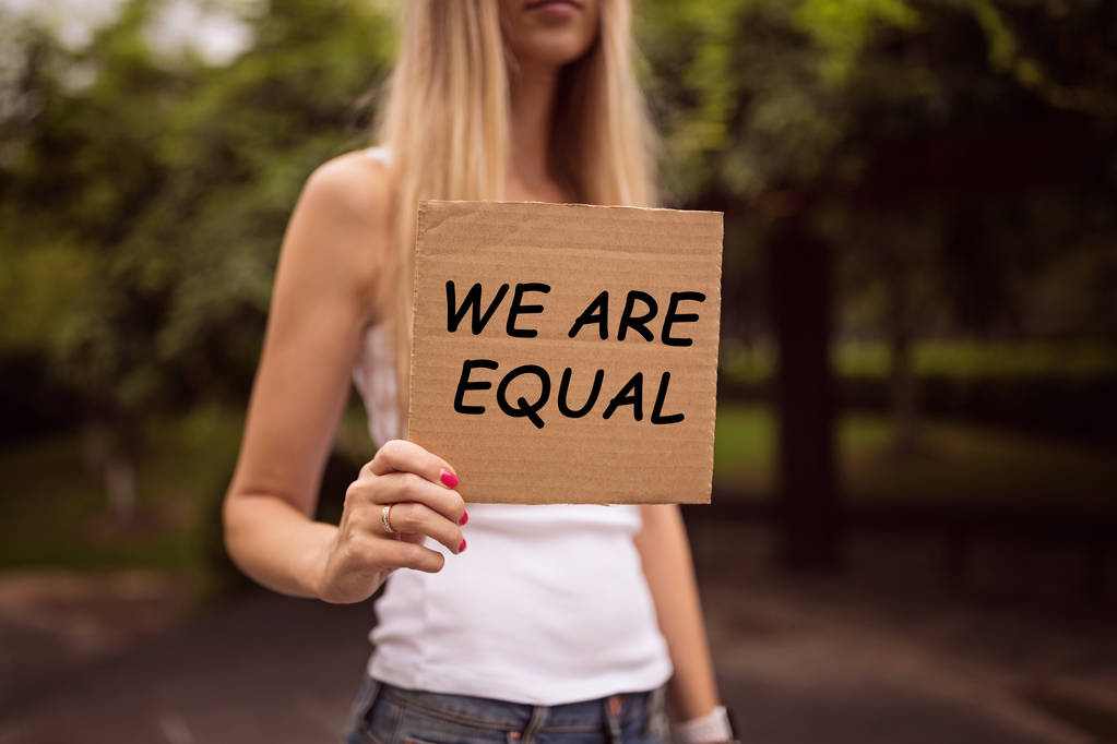 Концепция гендерного равенства как женщины держат в руках бумажный лист с надписью "Мы равны на фоне городской улицы". Женщина протестует на улице. Метафора социальной проблемы
. - Фото, изображение