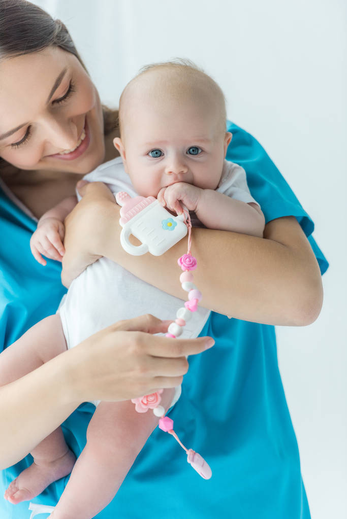 attraente e sorridente madre che tiene in braccio il suo bambino con giocattolo in ospedale
  - Foto, immagini