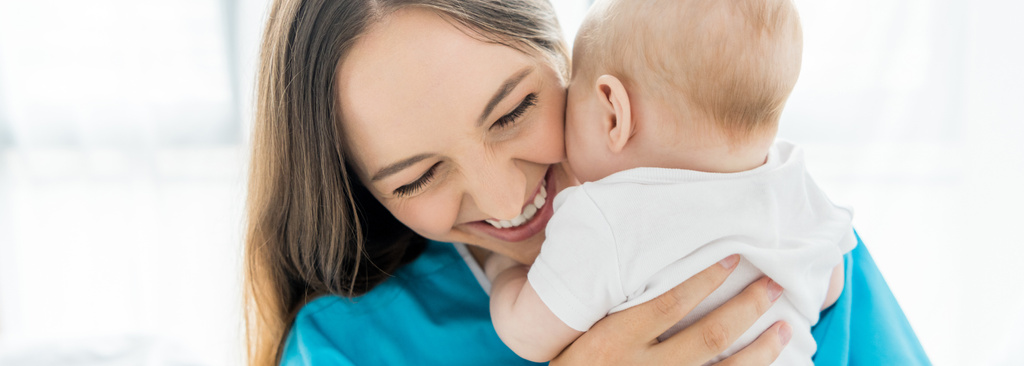  plano panorámico de madre atractiva y sonriente sosteniendo a su hijo en el hospital
  - Foto, Imagen