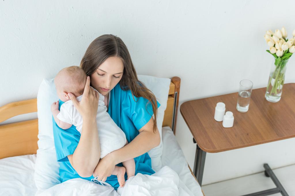 высокий угол обзора привлекательной и молодой матери, держащей своего ребенка в больнице
  - Фото, изображение