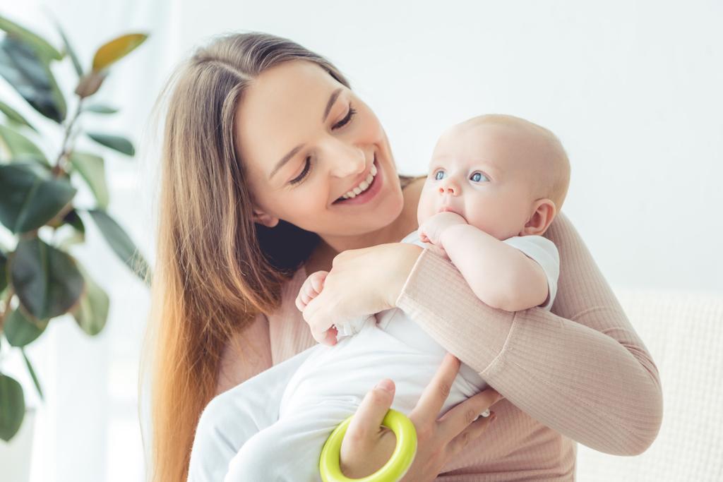 приваблива і усміхнена мати тримає іграшку і її дитину в квартирі
  - Фото, зображення