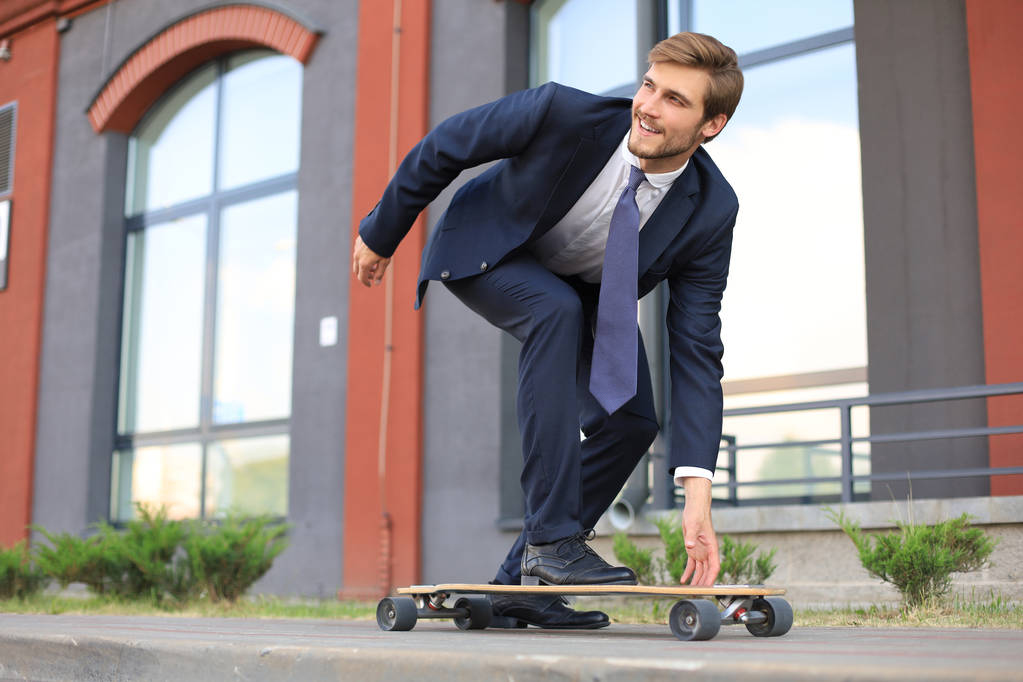 selbstbewusster junger Geschäftsmann im Businessanzug auf Longboard eilt in sein Büro, auf der Straße in der Stadt. - Foto, Bild