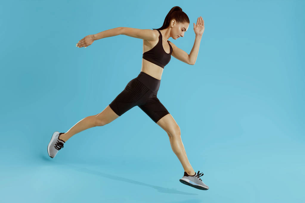 Sportlerin mit fittem Körper beim Springen und Laufen auf blauem Hintergrund - Foto, Bild
