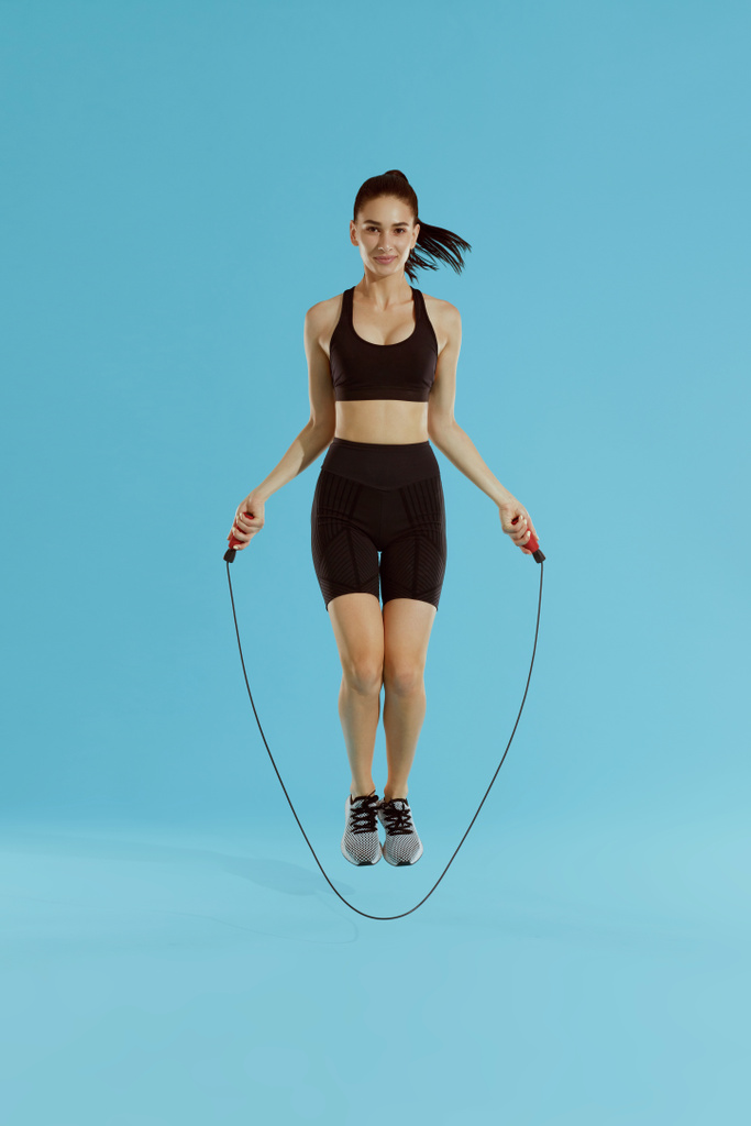 Фитнес. Женщина упражняется с скакалкой на синем фоне
 - Фото, изображение