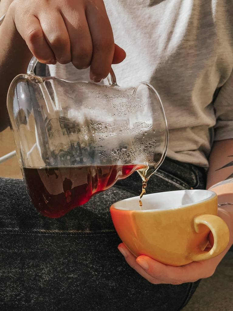 Вертикальный селективный снимок лица, наливающего чай в желтую керамическую чашку
 - Фото, изображение