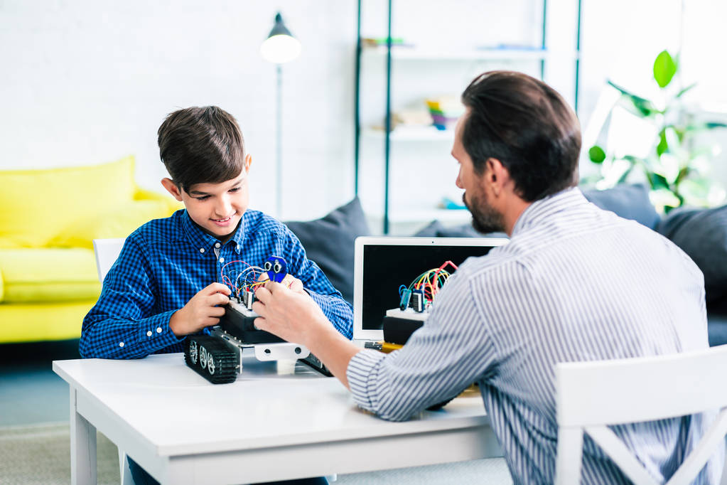 Miellyttävä mies ja hänen fiksu poikansa rakentamassa robottia istuessaan pöydässä
 - Valokuva, kuva