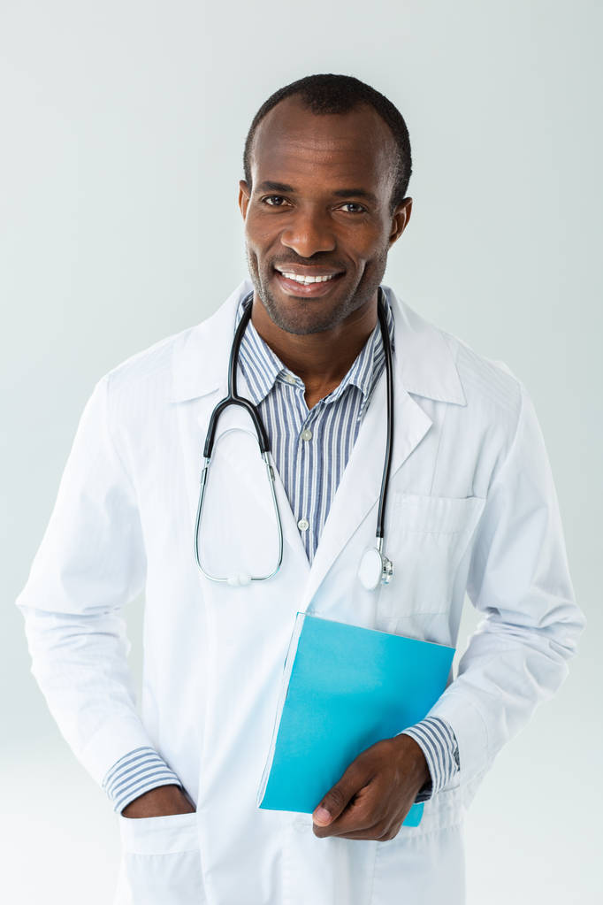 Αναφορά υπόθεσης. Χαρούμενος Αφροαμερικανός γιατρός που κρατά ένα ιατρικό ιστορικό ενώ εργάζεται σε ένα νοσοκομείο - Φωτογραφία, εικόνα