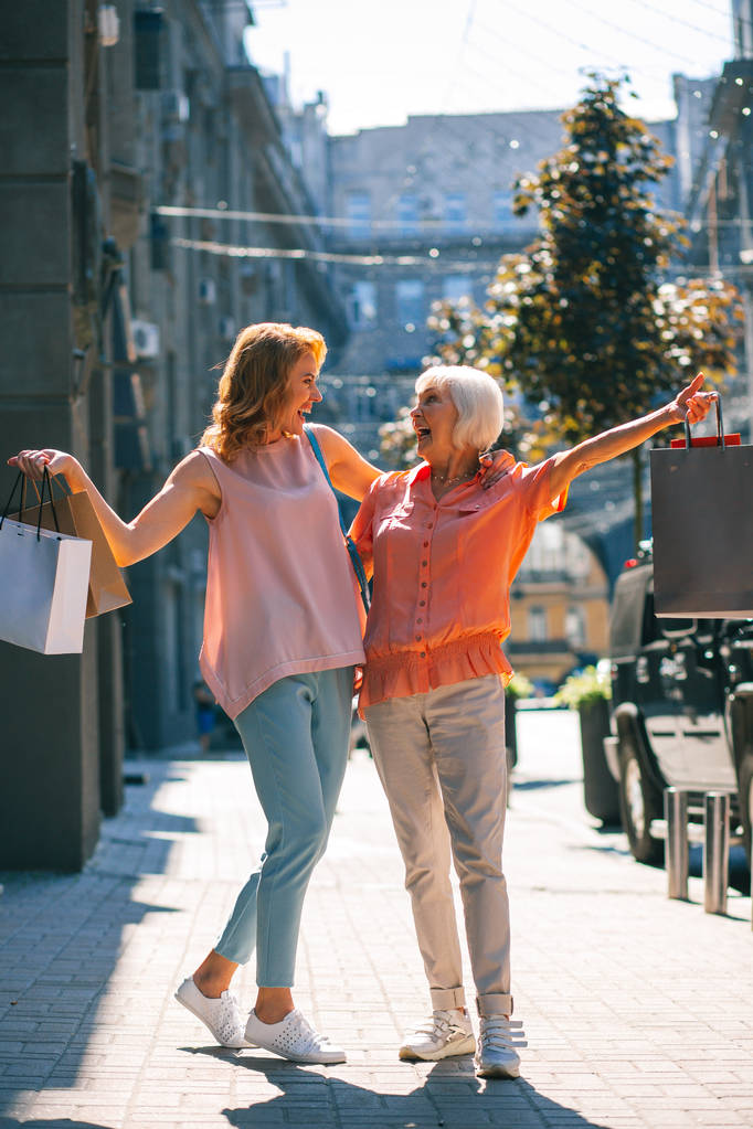 Dos mujeres alegres sonriéndose en la calle con bolsas en las manos
 - Foto, imagen