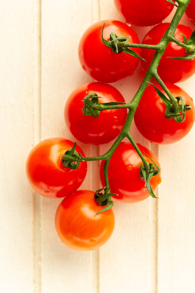 Top view photo of fresh ripe cherry tomatoes branch placed on the light striped wooden surface - Photo, Image