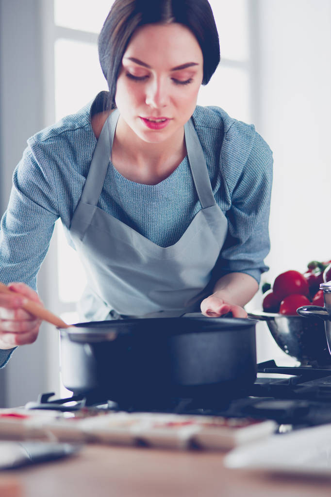 Femme debout près de la cuisinière dans la cuisine, cuisiner et sentir les beaux arômes
 . - Photo, image