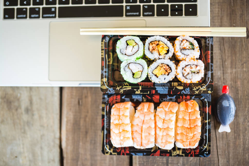 Rouleaux de sushi savoureux, crevettes et ordinateur portable à la table en bois. Livraison de nourriture. Espace de travail à la maison
 - Photo, image
