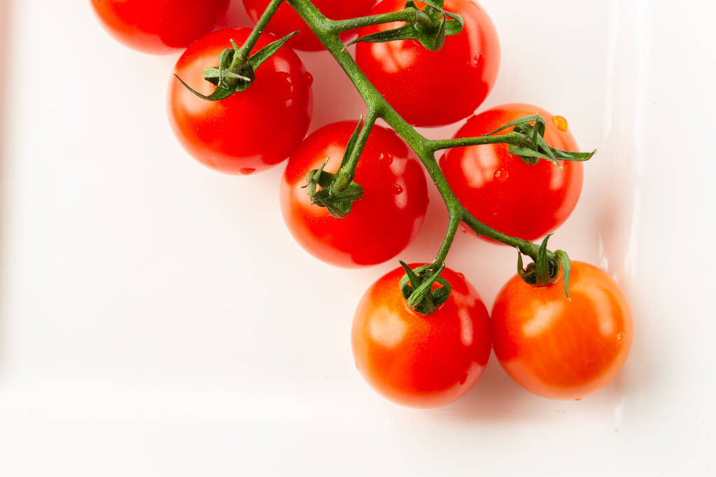 Top näkymä tuoreita maukkaita tomaatteja vihreällä oksalla makaa valkoinen levy ja näyttää puhtaalta
 - Valokuva, kuva