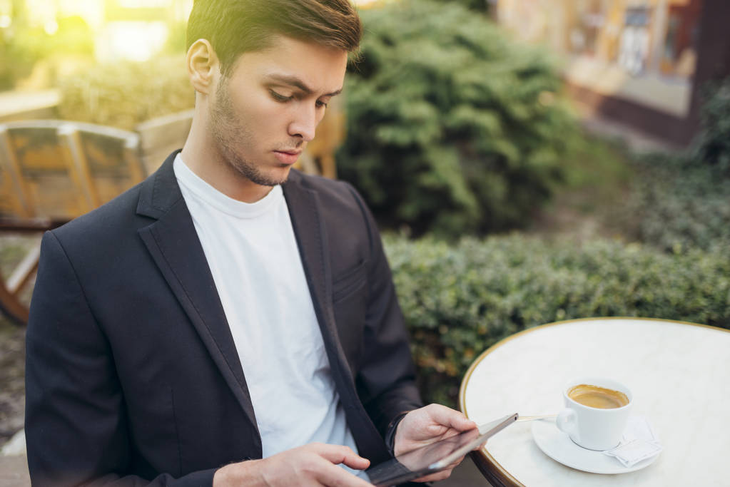 Technology and communication concept. Stylish Caucasian student surfing internet on digital tablet, enjoying free wireless connection at cafe during coffee break. Handsome male messaging online. - Photo, Image
