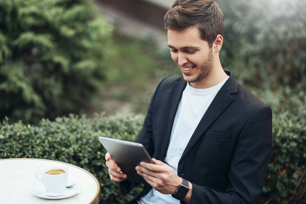 Ευτυχισμένο χαμογελαστή Καυκάσιος επιχείρηση άνθρωπος κρατώντας συσκευή tablet περιήγηση στο διαδίκτυο και διαβάζοντας καλά νέα σχετικά με το email κατά τη διάρκεια του διαλείμματος καφέ στο μοντέρνο καφέ στην πόλη. Έννοια της τεχνολογίας και των επιχειρήσεων. - Φωτογραφία, εικόνα