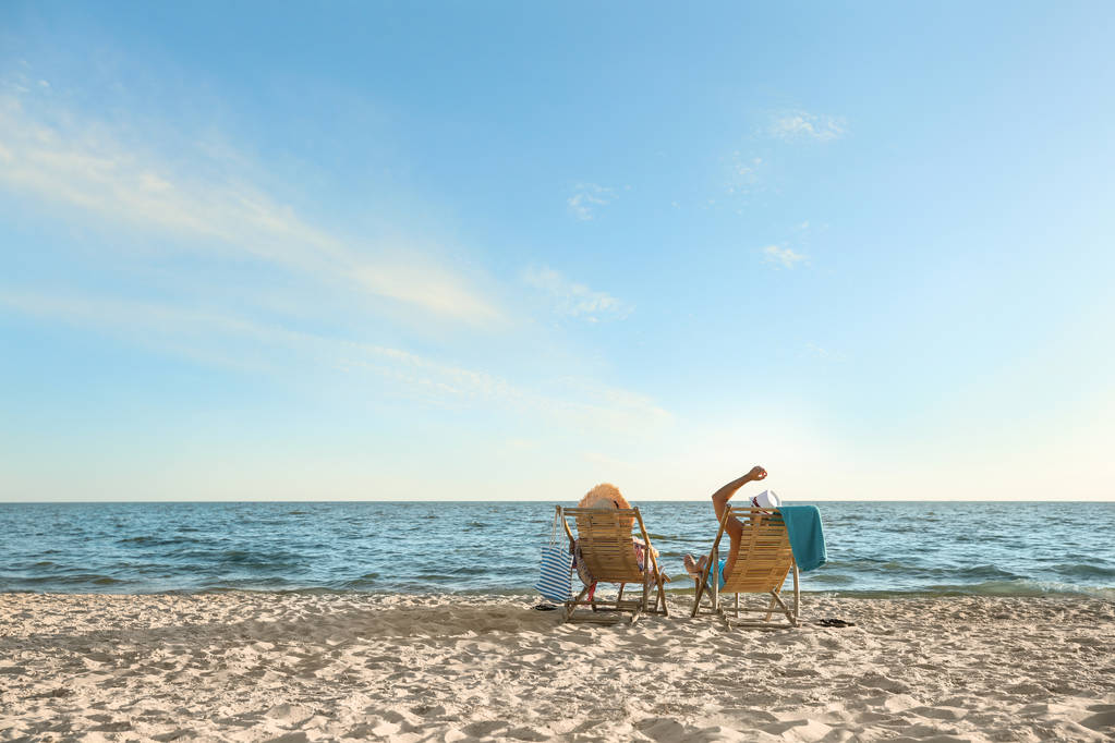 Νεαρό ζευγάρι χαλαρωτικό στο κατάστρωμα καρέκλες στην παραλία κοντά στη θάλασσα - Φωτογραφία, εικόνα