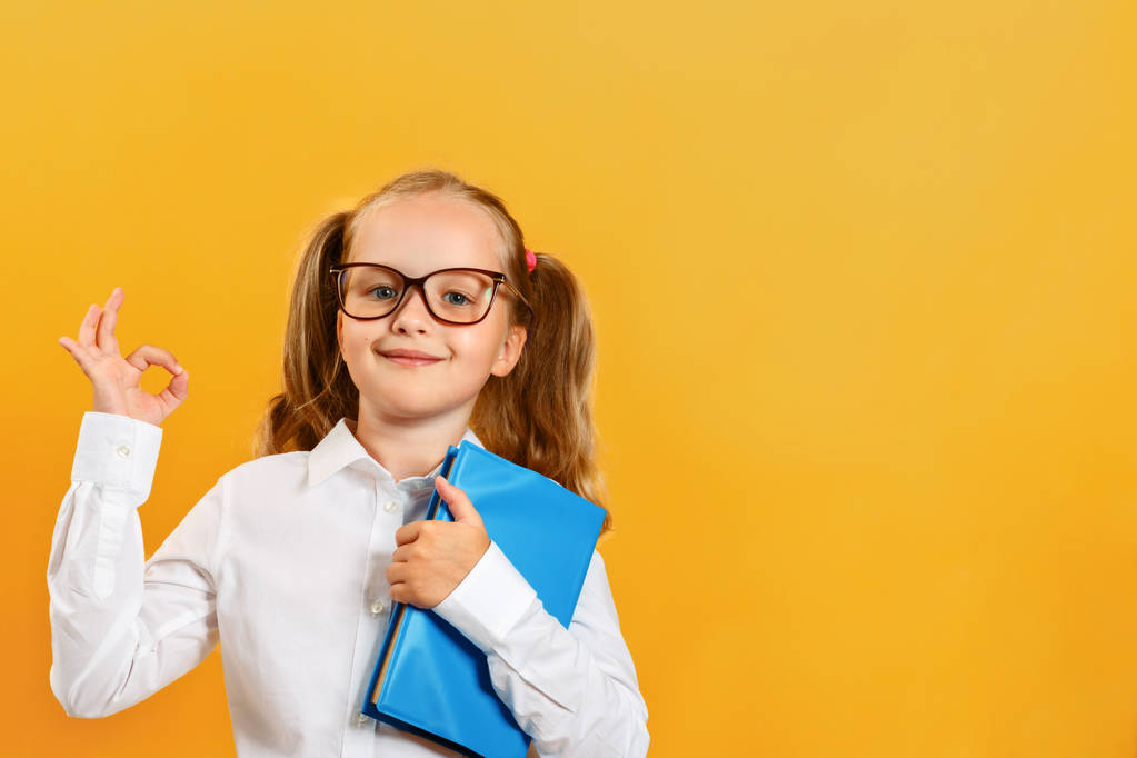 De vuelta a la escuela. Una linda niña con un libro en gafas muestra un cartel de aprox. El concepto de éxito y educación
 - Foto, imagen