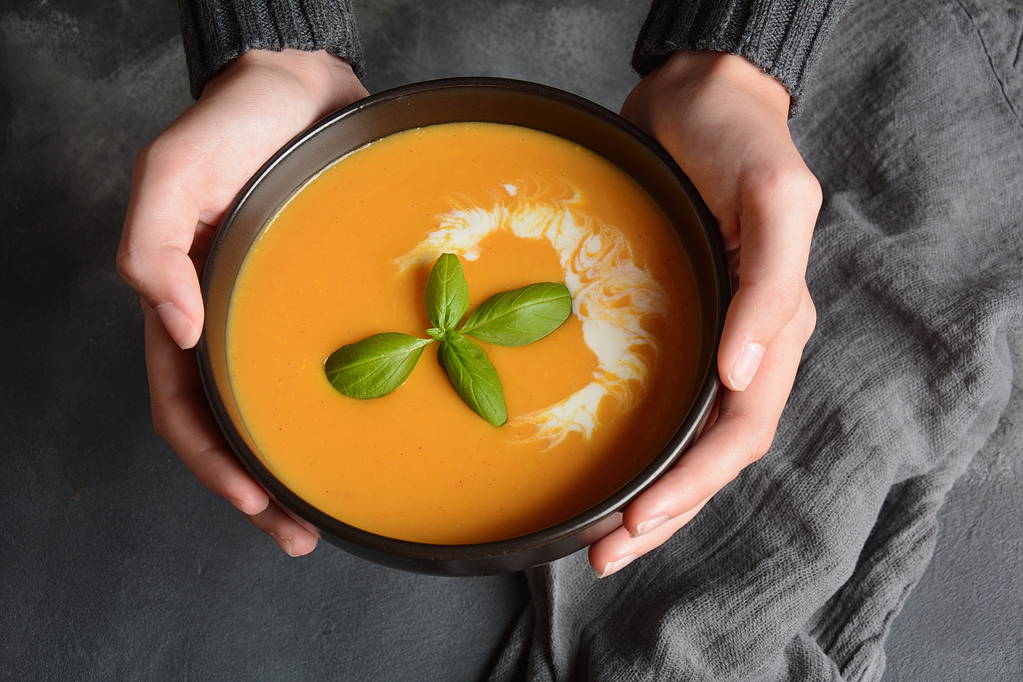 Tigela de sopa de creme de abóbora e cenoura nas mãos. Outono conceito sopa vegan quente
 - Foto, Imagem
