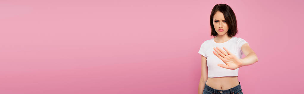 plano panorámico de hermosa chica seria mostrando gesto de stop aislado en rosa
 - Foto, imagen