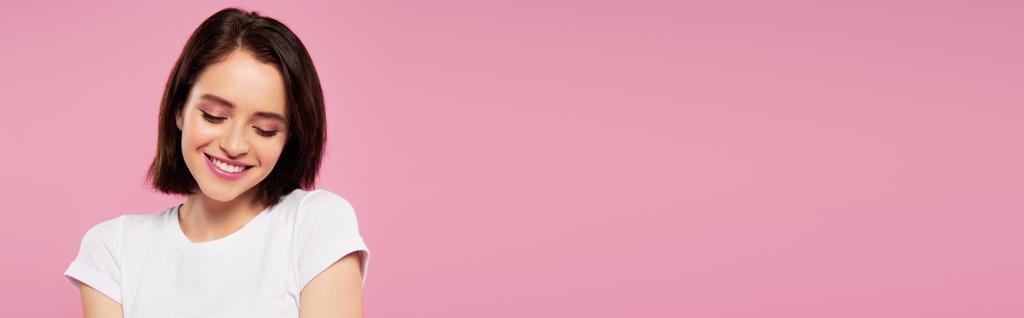 plano panorámico de hermosa chica tímida sonriente mirando hacia abajo aislado en rosa
 - Foto, Imagen