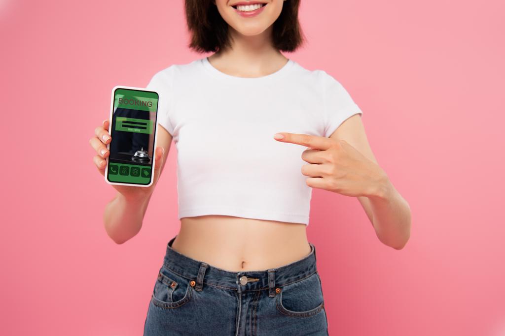 recortado vista de chica apuntando con el dedo en el teléfono inteligente con aplicación de reserva aislado en rosa
 - Foto, imagen