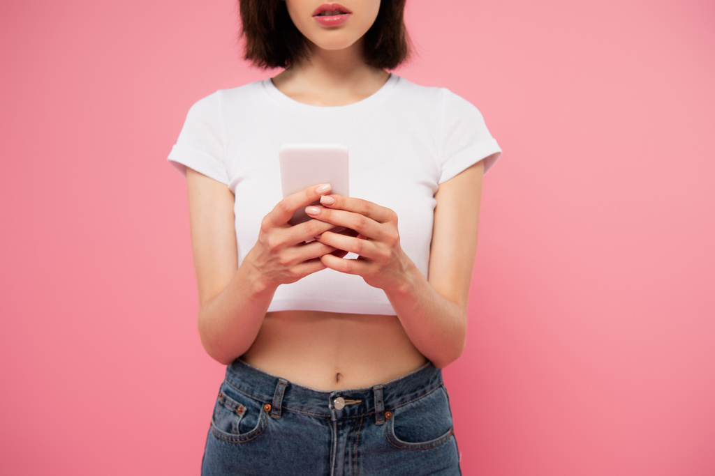 recortado vista de chica mensajes de texto en el teléfono inteligente aislado en rosa
 - Foto, Imagen