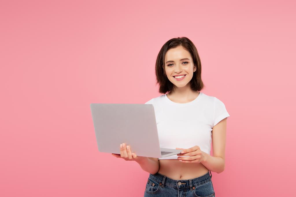 glimlachend mooi meisje houden laptop geïsoleerd op roze - Foto, afbeelding