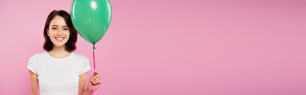 ピンクに隔離された緑の風船を保持している笑顔のかわいい女の子のパノラマショット - 写真・画像