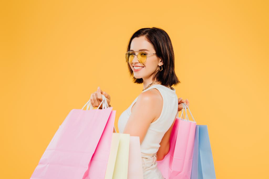 Glücklich lächelnde Frau mit Sonnenbrille und Einkaufstüten auf gelbem Grund - Foto, Bild