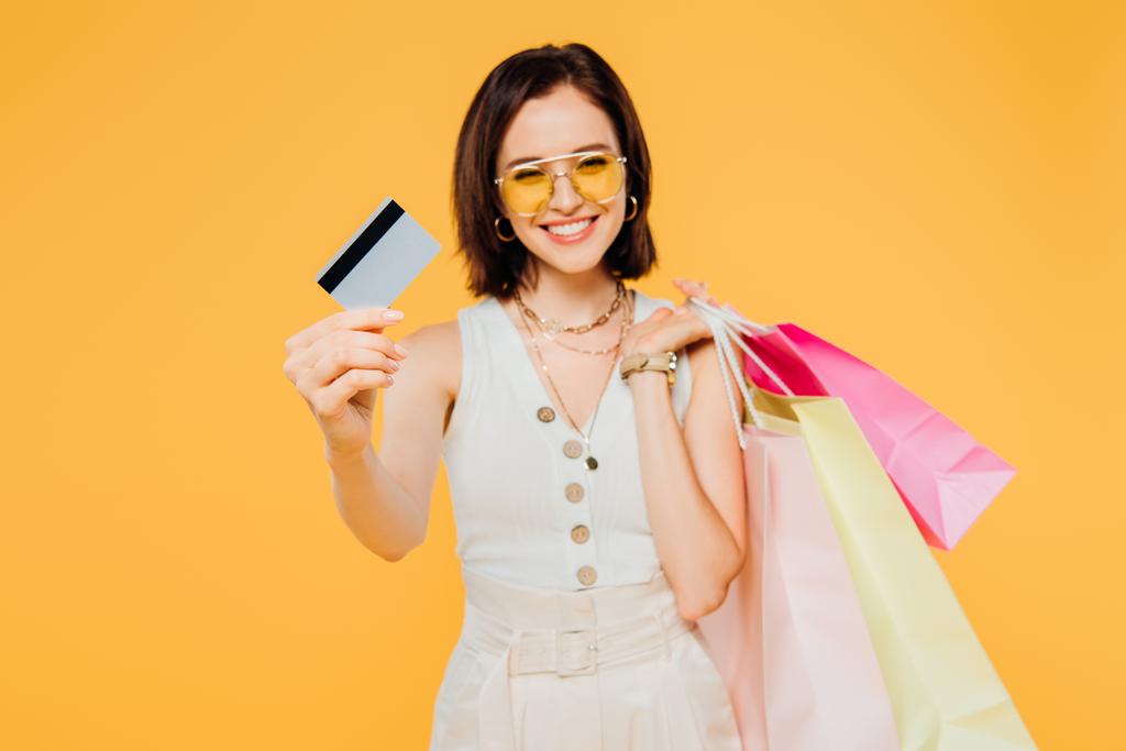 felice ragazza in occhiali da sole con shopping bags presentando carta di credito isolata su giallo
 - Foto, immagini