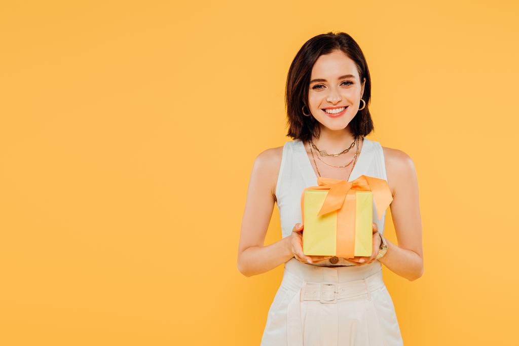 šťastná usměvavá dívka držící dárkovou schránku izolovanou na žluté - Fotografie, Obrázek