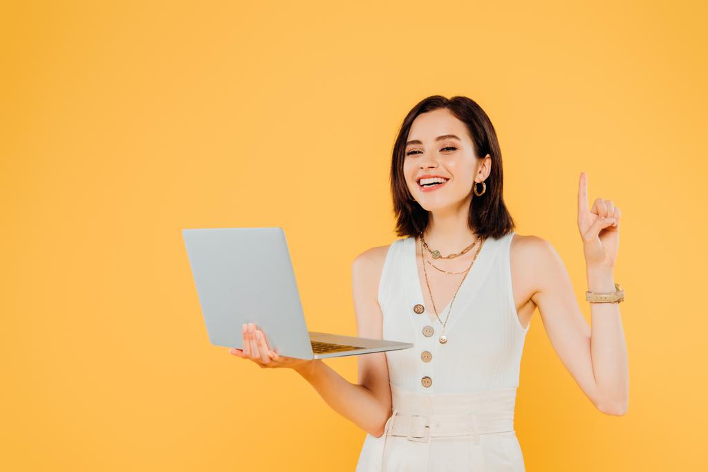 smiling elegant girl with laptop showing idea gesture isolated on yellow - Photo, Image