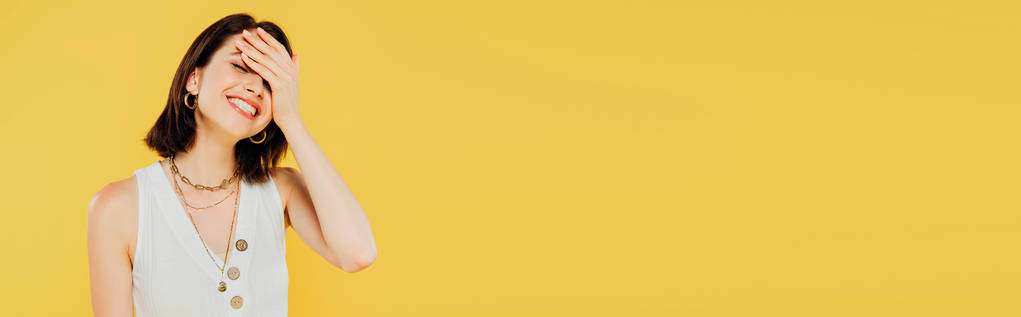 панорамный снимок улыбающейся элегантной девушки с рукой на голове, изолированной на желтом
 - Фото, изображение