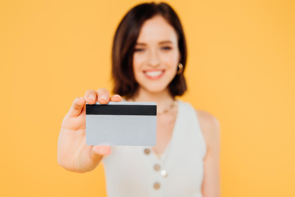 sarı izole kredi kartı tutan gülümseyen zarif kız seçici odak - Fotoğraf, Görsel
