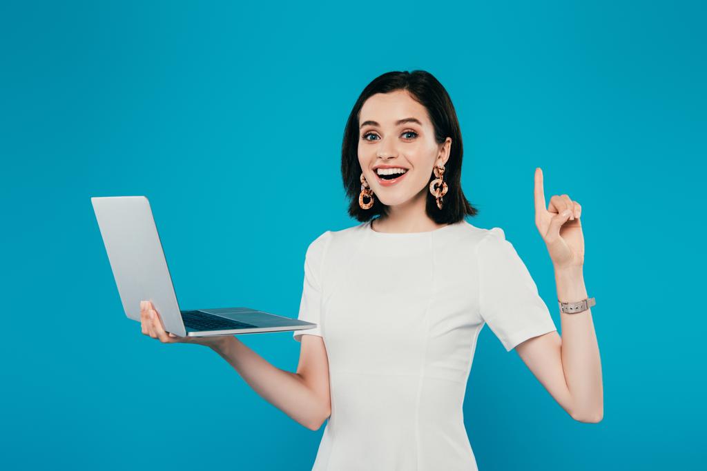 opgewonden glimlachend elegante vrouw houdt laptop en toont idee gebaar geïsoleerd op blauw - Foto, afbeelding