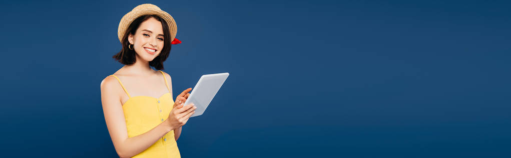 plano panorámico de chica bonita sonriente en sombrero de paja sosteniendo tableta digital aislado en azul
 - Foto, Imagen