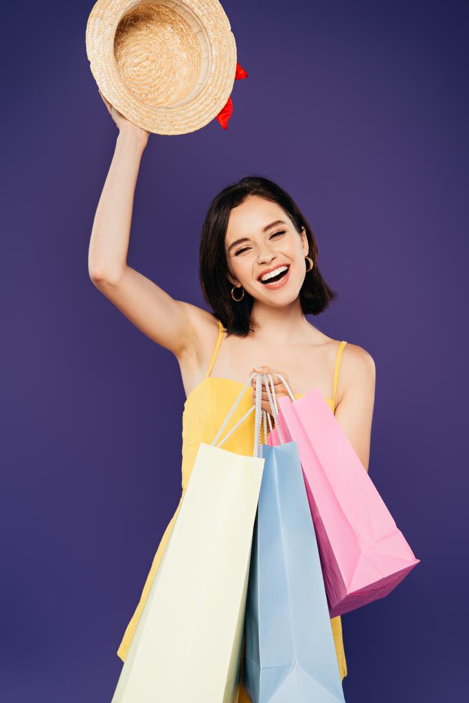 mosolyogva lány bevásárló táskák gazdaság Szalmakalapot izolált lila - Fotó, kép