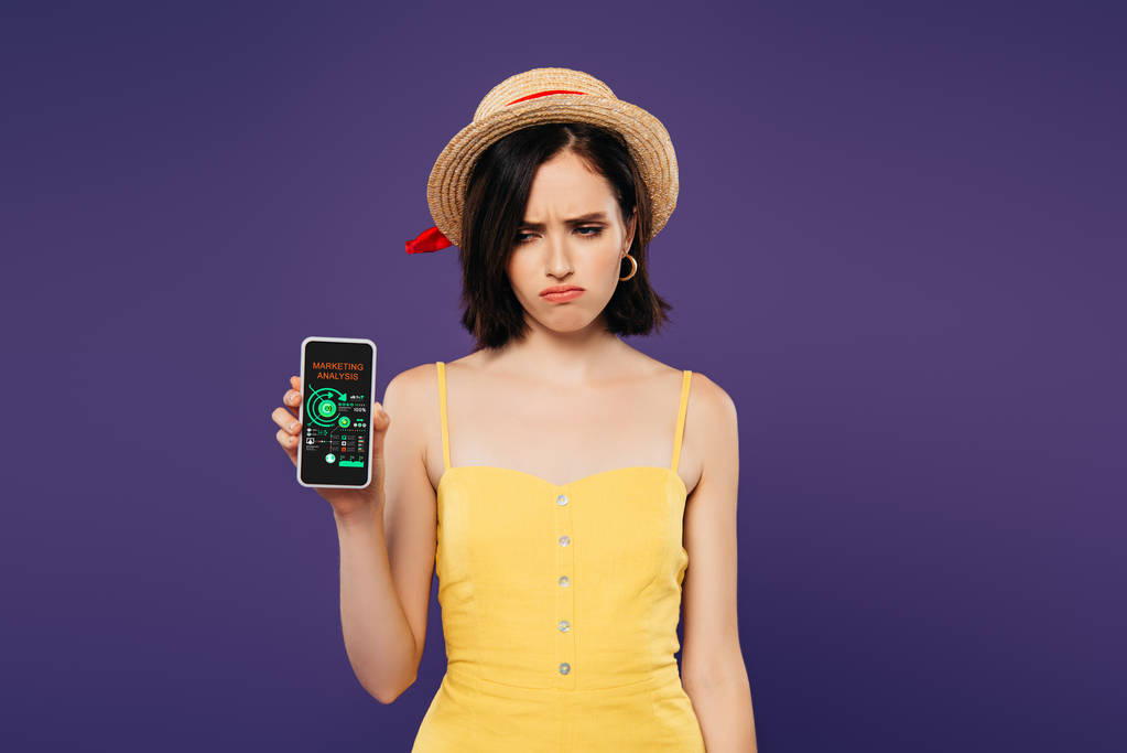 сумна красива дівчина в солом'яному капелюсі тримає смартфон із додатком маркетингового аналізу ізольовано на фіолетовому
  - Фото, зображення