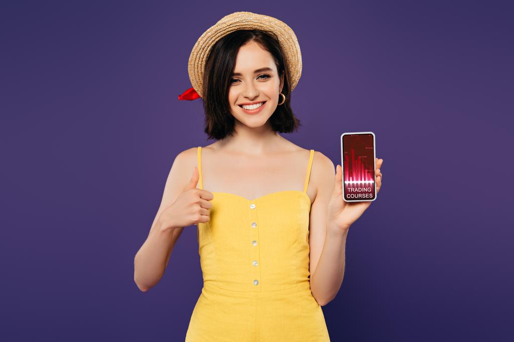 sonriente chica bonita en sombrero de paja que muestra el pulgar hacia arriba mientras sostiene el teléfono inteligente con la aplicación cursos de comercio aislado en púrpura
  - Foto, imagen