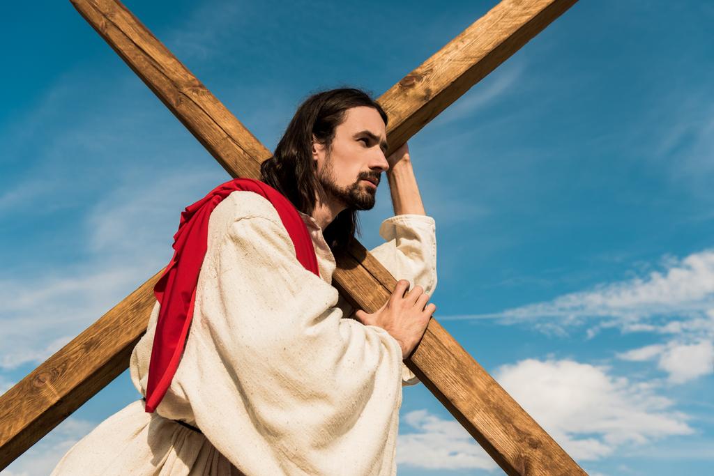 pohled nízkého úhlu vousatého muže, který drží kříž proti modrému nebi  - Fotografie, Obrázek