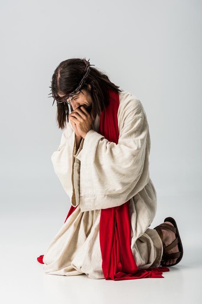 bärtiger Mann im Kranz betet auf Knien auf grau  - Foto, Bild