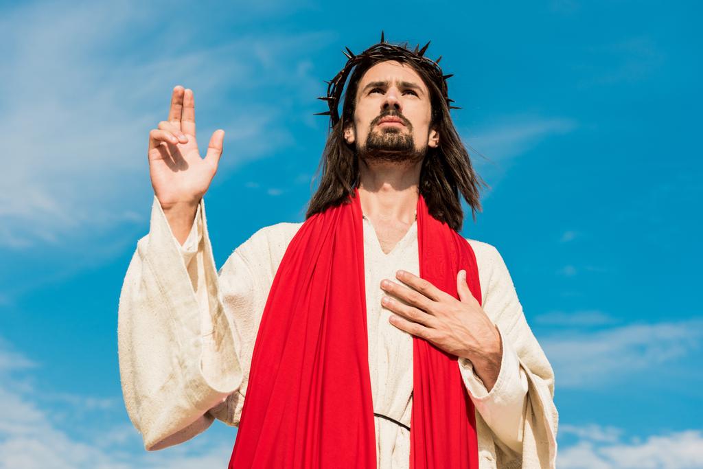 baixo ângulo de visão de jesus orando com a mão no peito
  - Foto, Imagem