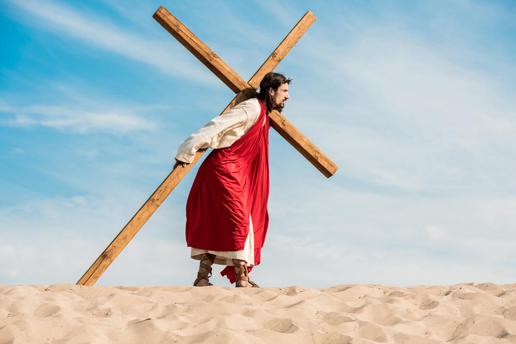 homem barbudo em grinalda andando com cruz no deserto
  - Foto, Imagem