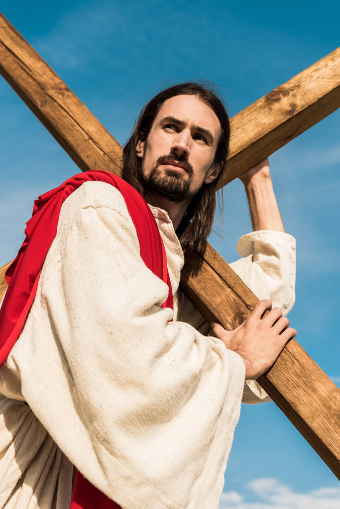 青空に対して十字架を持つイエスの低い角度の図  - 写真・画像