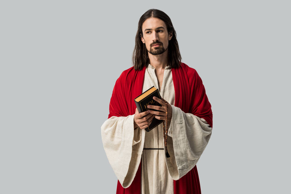 handsome man looking at camera while holding holy bible isolated on grey  - Photo, Image